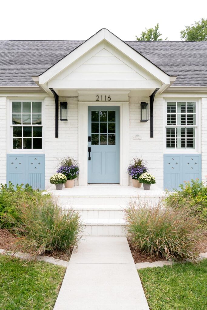 Charming white brick house with blue door and manicured garden © Nashville Interiors