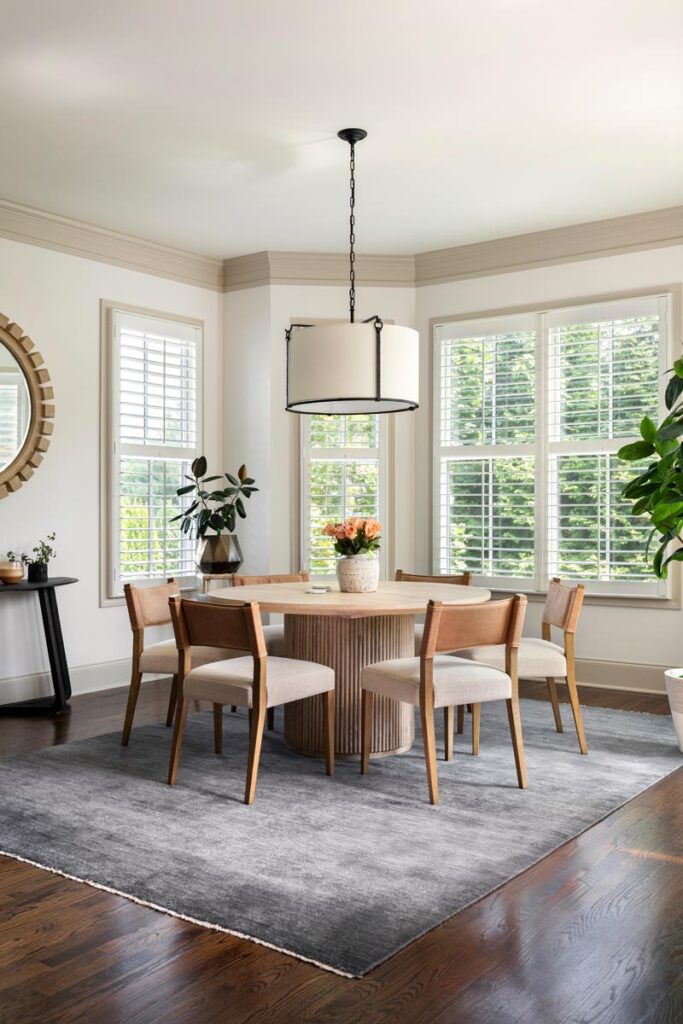 Modern dining room with round table, wooden chairs, and large windows © Nashville Interiors