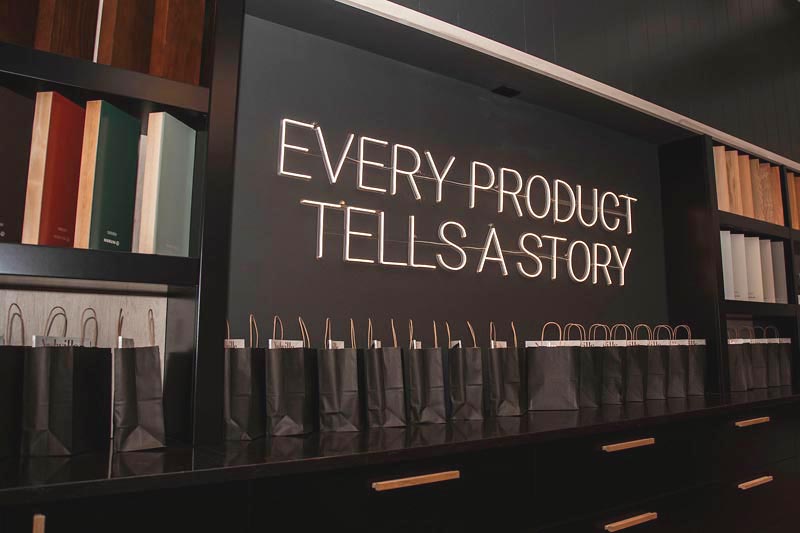 Illuminated sign on wall reads 'Every Product Tells a Story' with bags below Photo by Nashville Interiors