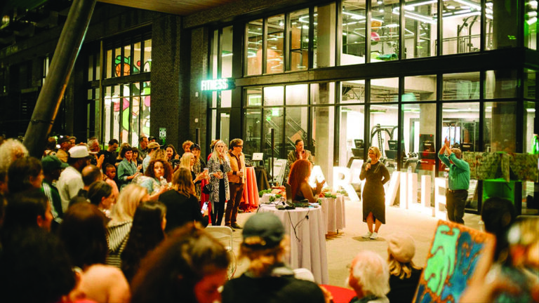 Crowd at gallery exhibition opening with art displays and event speakers Photo by Nashville Interiors