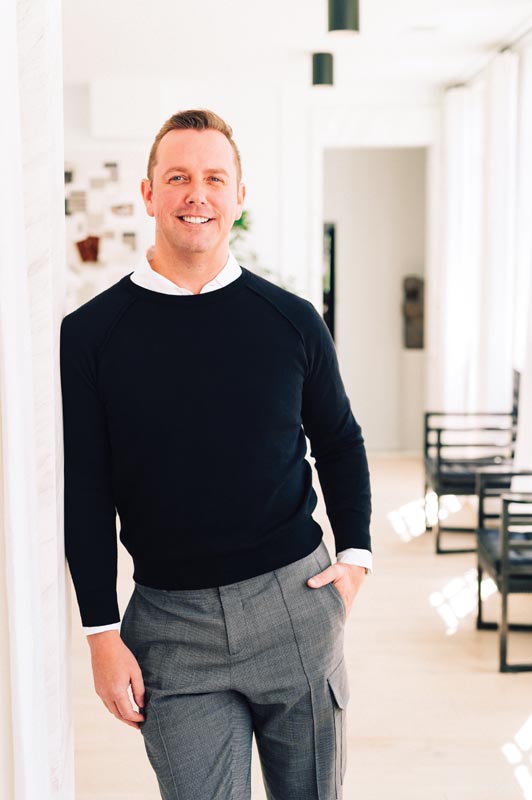 Smiling man in modern living room wearing a black sweater and gray pants Photo by Nashville Interiors